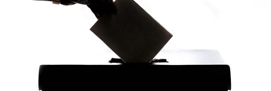 Silhouette of a hand placing a vote into a ballot box, symbolizing democracy.