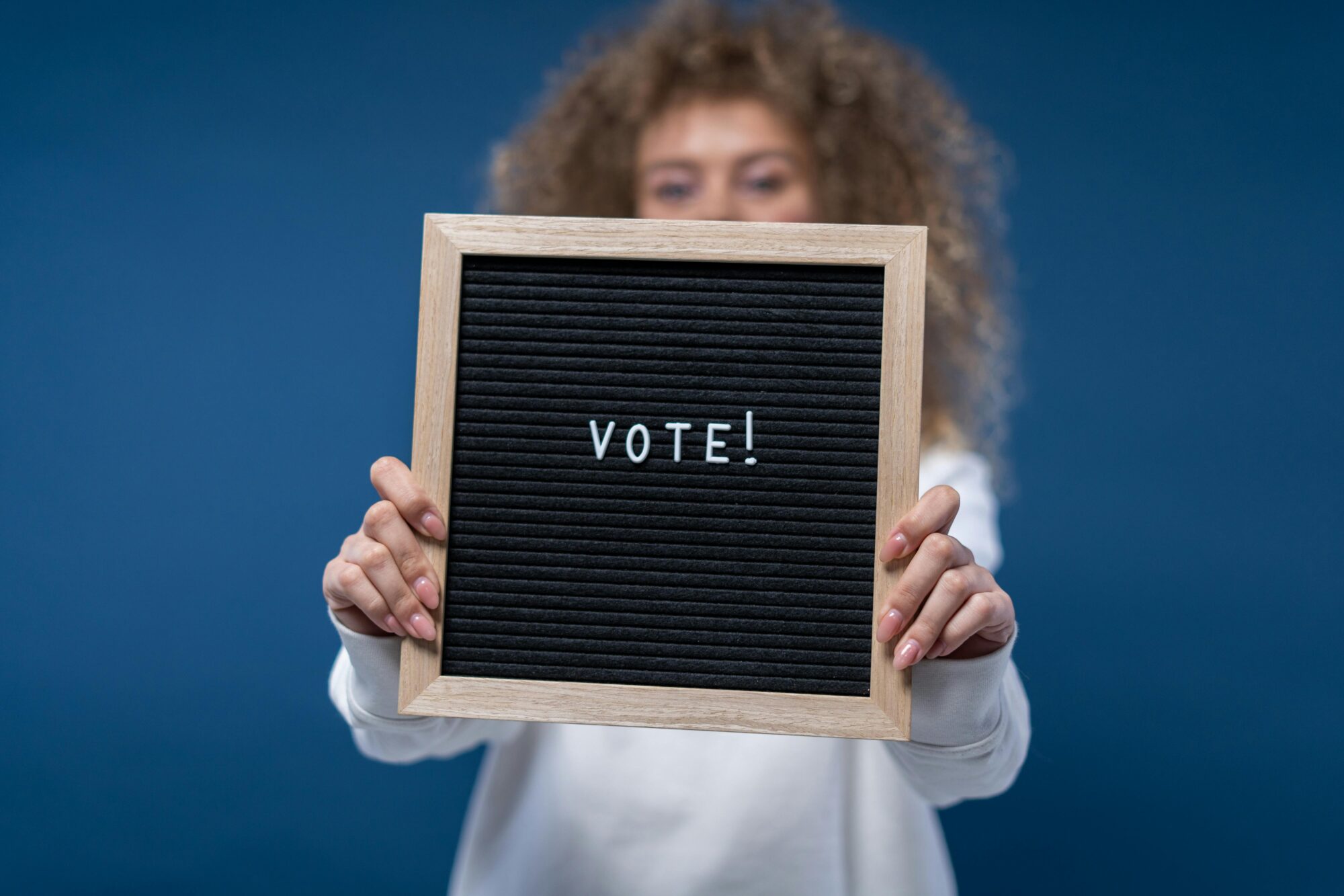 Woman holding a wooden framed board with 'Vote!' text, highlighting democratic participation.