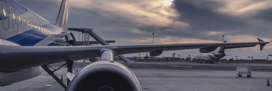 A passenger airplane is parked on the tarmac at sunset, with another aircraft in the background.